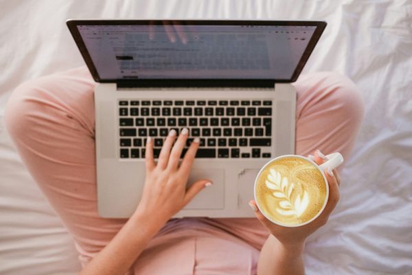 person using MacBook Pro and holding cappuccino