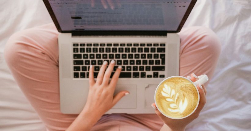 person using MacBook Pro and holding cappuccino