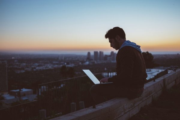 man sitting on concrete brick with opened laptop on his lap