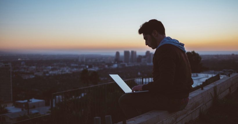 man sitting on concrete brick with opened laptop on his lap